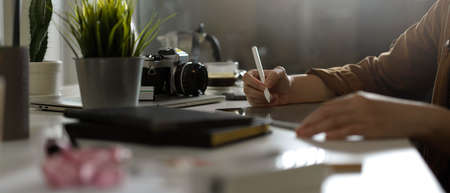Side view of female photographer working with mock up tablet on table with camera and supplies in studioの写真素材