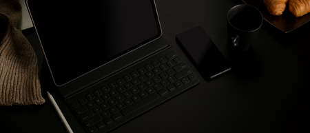 Cropped shot of dark home office with croissants, coffee up, digital tablet, smartphone and supplies...
