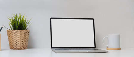 Close up view of simple home office with mock up laptop, coffee cup, plant pot and stationery on white deskの写真素材