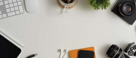 Overhead shot of modern workspace with copy space, digital devices, coffee cup, schedule book and decorations on white deskの写真素材