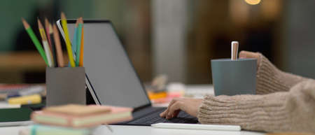 Side view of female student doing assignment with mock up tablet and stationery while holding cup on...