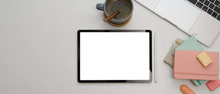 Top view of study table with mock up tablet, laptop, notebooks, stationery and coffee cup on white deskの写真素材