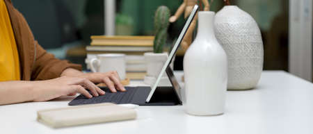Side view of female typing on tablet keyboard on worktable with decorations and stack of books