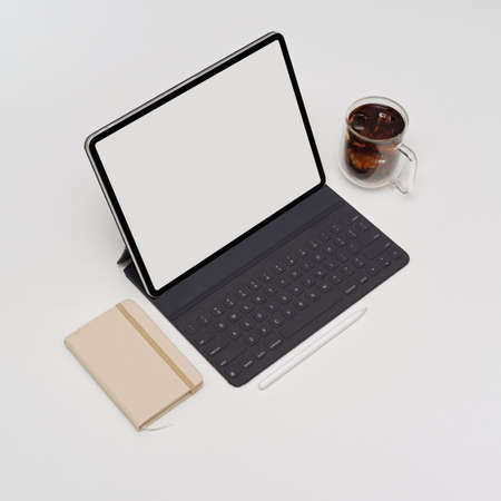 Cropped shot of blank screen tablet with keyboard on white table with diary book and coffee cup