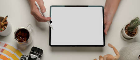 Overhead shot of male hands using mock up tablet on worktable with camera, supplies and decorations