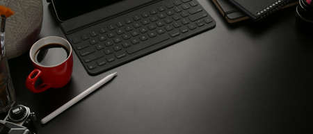 Cropped shot of dark office desk with digital tablet, coffee mug, supplies and copy space on black tableの写真素材