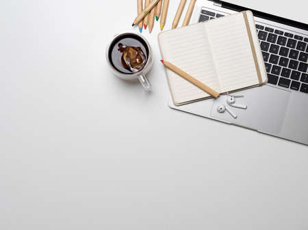Top view of workspace with laptop, opened notebook, stationery, coffee cup and copy space on white...