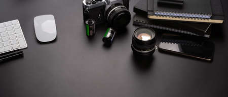 Cropped shot of dark office desk with copy space, camera, computer device, smartphone, stationery and accessoriesの写真素材