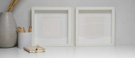 Close up view of workspace with mock up frames, stationery, ceramic vase and copy space on white...