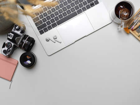Top view of workspace with copy space, laptop, camera, stationery, supplies and decorations on white...