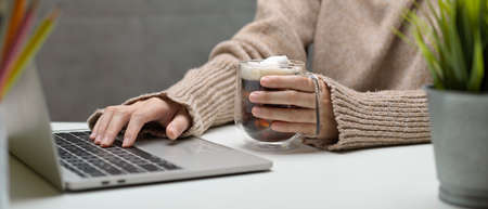 Side view of female working with laptop and holding a cup of beverage on white worktableの写真素材