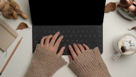 Overhead shot of female typing on digital tablet keyboard on worktable with stationery, beverage and...