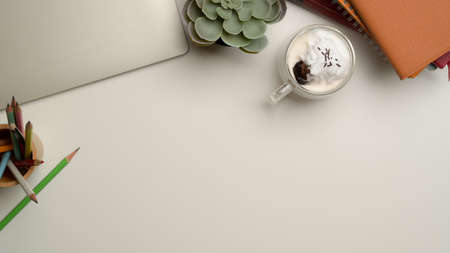 Top view of workspace with copy space, laptop, books, stationery, cup of beverage and tree pot on white deskの写真素材
