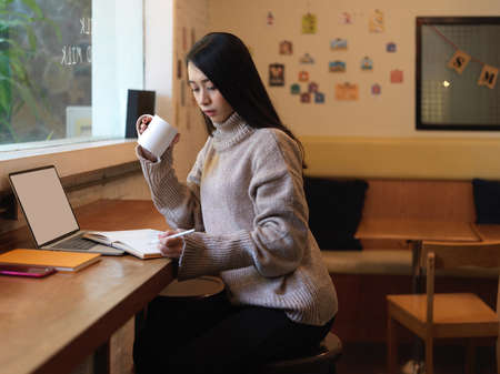 Side view of female resting with drinking hot beverage while working on wooden counter bar in cafe