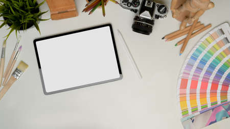 Top view of tablet on work table with paint tools, camera, stationery and copy space