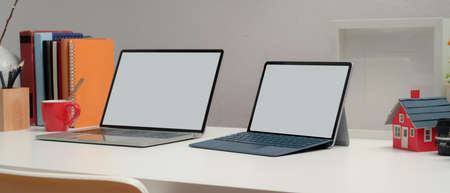 Cropped shot of two blank screen laptop on office desk with books and decorations in home office...