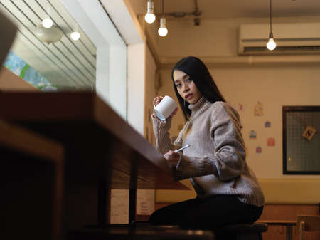 Cropped shot of female resting with drinking hot beverage while working on wooden. counter bar in...