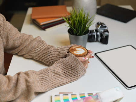 Side view of female in sweater holding a cup of beverage on office desk  digital tablet,  .の写真素材