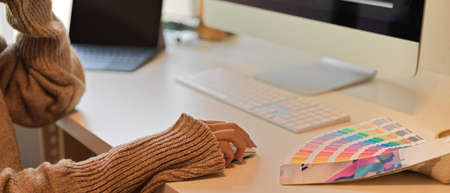Side view of female in sweater using computer device on white desk in office room