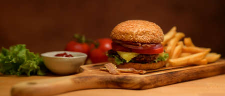 Close up view of fresh tasty homemade bacon burger with french fries on wooden tray serving with...