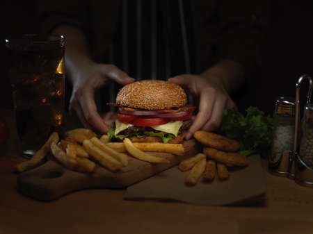 Close up view of female cook arranging fresh tasty gilled burger on wooden tray ready to serve with french friesの写真素材