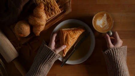 Overhead shot of female having breakfast with freshly baked delicious bakery and latte coffee on wooden tableの写真素材