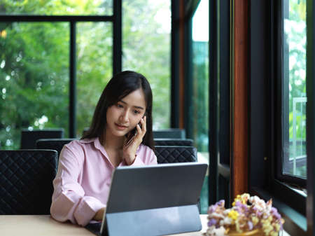 Cropped shot of businesswoman talking on phone while working with digital tablet on table in cafeteriaの写真素材