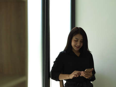 Portrait of female teenager using smartphone while standing against glass wall