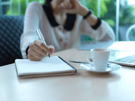 Close up view of female office worker taking note on blank notebook on wooden table in meeting room