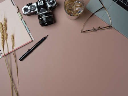 Top view of workspace with stationery, laptop, camera, glasses and copy space on pink desk