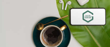 Top view of coffee table with mock up smartphone, wireless earphone, coffee cup and leaves decorated on tableの写真素材