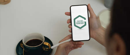 Close up view of female hands using mock up smartphone while relaxing with hot coffee