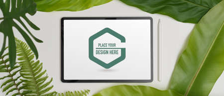 Top view of mock up digital tablet and stylus on white background decorated with green leavesの写真素材