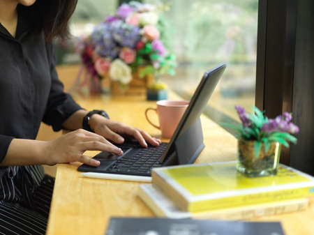 Side view of female freelancer using digital tablet with keyboard on counter bar in cafeteriaの写真素材