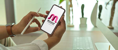 Cropped shot of male entrepreneur showing mock up screen smartphone while sitting in workplace