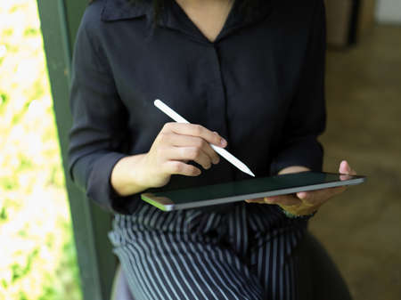 Cropped shot of female office worker relaxed sitting near glass window and using digital tabletの写真素材