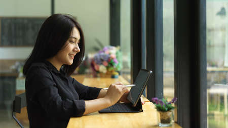 Side view of female working with digital tablet on wooden bar beside glass window in cafe