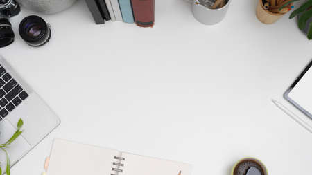Top view of workplace with copy space, laptop, tablet, notebook, books and stationery on white table