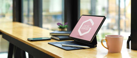 Side view of portable workspace with mock up digital tablet, supplies and coffee mug on wooden bar
