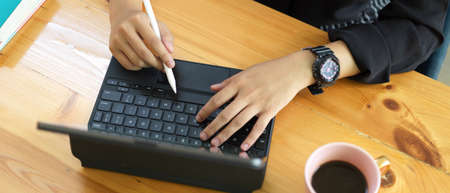 Overhead shot of female hands using digital tablet with stylus and keyboard on wooden desk