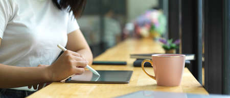 Side view of female hand using digital tablet on wooden bar beside window in cafe