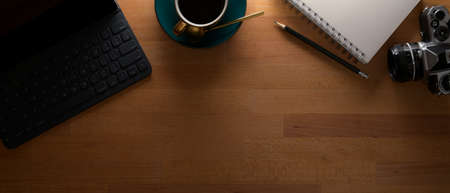 Top view of workspace with tablet keyboard, camera, diary book, coffee cup and copy space on wooden...