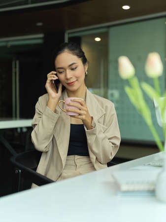 Portrait of female entrepreneur talking on the phone while take a coffee break in office roomの写真素材