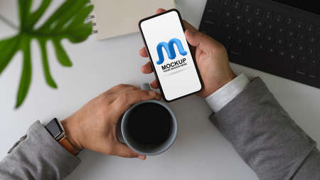 Overhead shot of male entrepreneur take a break with coffee and mock up smartphone on office deskの写真素材