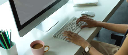 Cropped shot of female office worker working on computer with stationery and coffee cup on office...