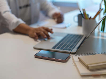 Cropped shot of male hand using laptop while taking note on notebook on worktable in home office...