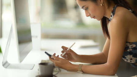 Side view of female fashion designer using smartphone while working on office deskの写真素材