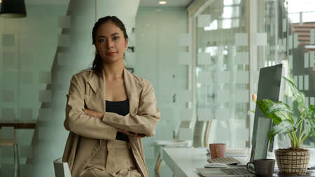 Portrait of female entrepreneur arms crossed and smiling while sitting in glass wall office roomの写真素材