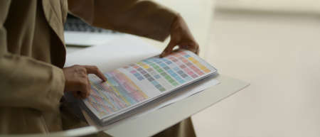 Side view of female fashion designer choosing colour on colour chart while sitting in office room