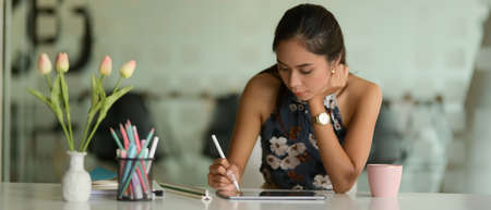 Portrait of female entrepreneur working with digital tablet on working table with stationery and...